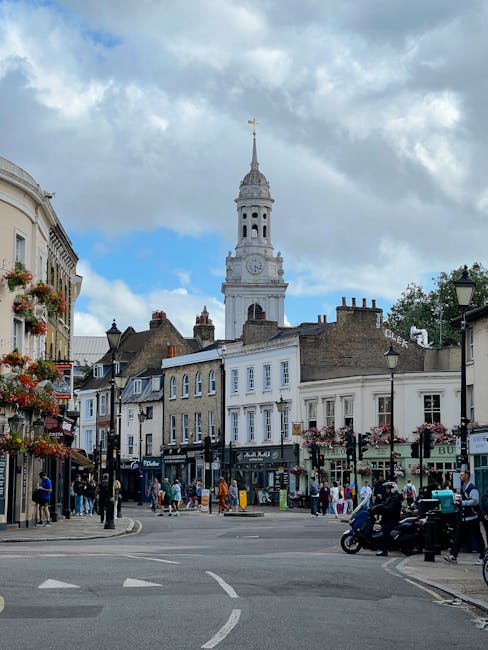 The image shows a lively street scene in Haringey with a prominent historic clock tower featuring a tall spire and a clock face, surrounded by a mix of Georgian and Victorian-style buildings. On the l