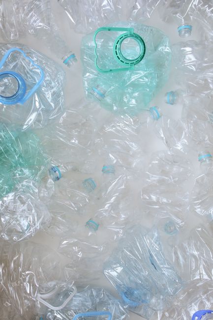 A collection of transparent plastic water bottles, some with blue and green caps, scattered across a surface. The bottles vary in size and appear to be empty, with some crushed or partially collapsed.